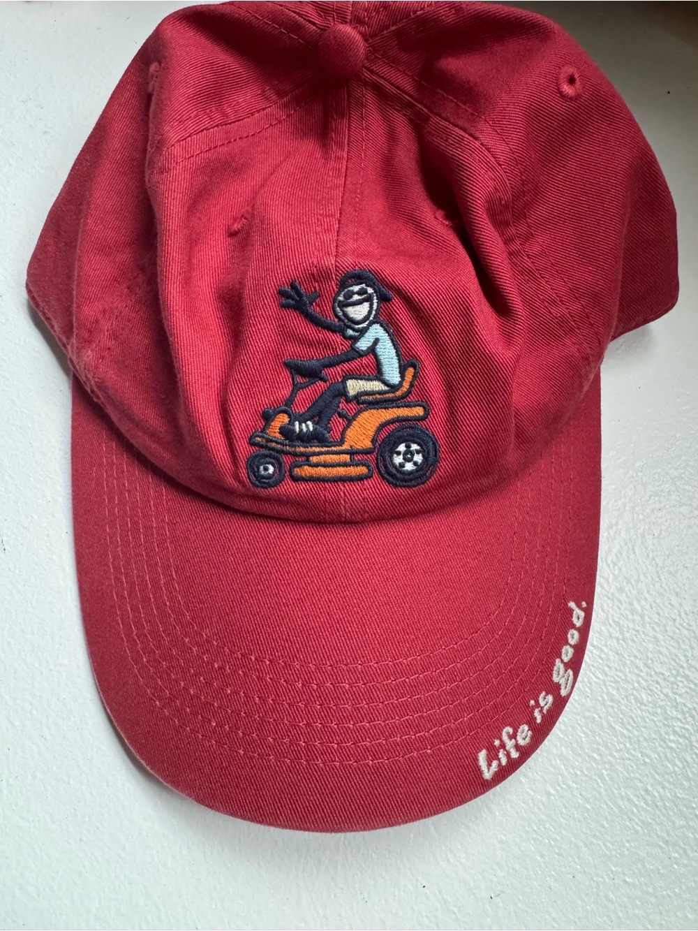 Life is Good Hat Adirondack riding a lawnmower.